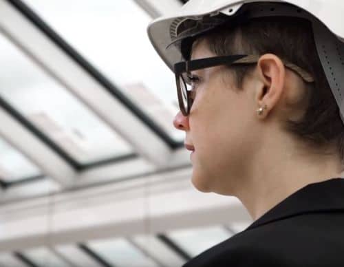 Sceenshot from a movie of a woman in a construction hat in a glass building