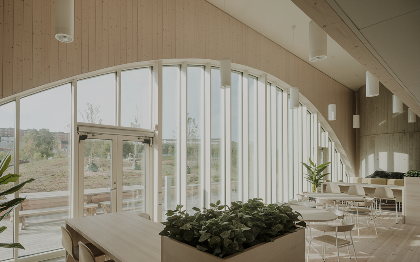 Interior image of a bright lunchroom with large windows, wood panels, plants and modern furniture.